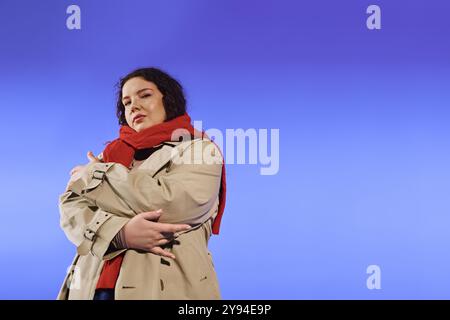 Eine selbstbewusste Frau in Übergröße umschmeichelt ihre Schönheit, während sie vor einem auffälligen blauen Hintergrund steht. Stockfoto