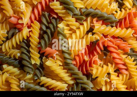 Ungekochte Fusilli Pasta in leuchtenden Farben: Eine faszinierende kulinarische Leinwand aus bunten Spiralen, die einen lebendigen und strukturierten Hintergrund für Gourmet-Kochen schafft. Farbige Trockene Pasta. Rohe Makkaroni Stockfoto