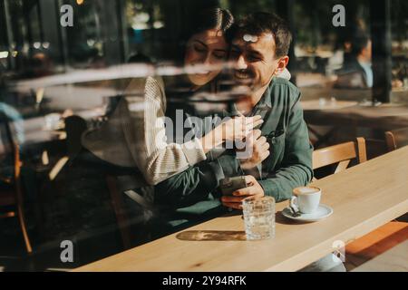 Junge Paare teilen sich zärtliche Momente in einem Café, umgeben von Grün und natürlichem Licht, während sie sich bei warmen Getränken und verspielten Gesten verbinden Stockfoto