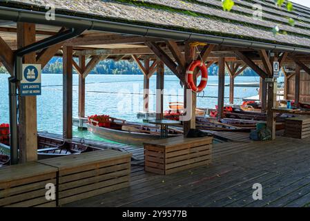 Hafenblick mit Holzbooten zur Miete an einem Bootssteg im See Bled. Wir können sehen, dass rote Rettungswesten und Schwimmwesten ebenfalls erhältlich sind. Mit diesen Gefäßen Stockfoto