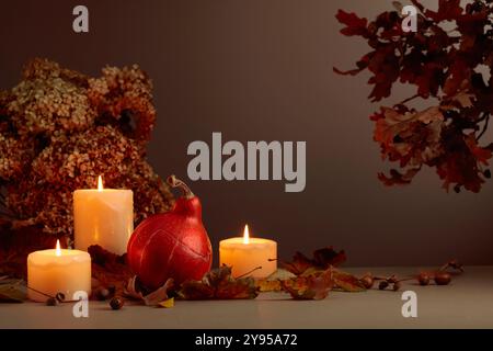 Stillleben mit Kürbis, ausgetrockneten Blättern und brennenden Kerzen. Im Hintergrund getrocknete Hortensienblüten und Eichenzweige. Herbstkonzept. Stockfoto