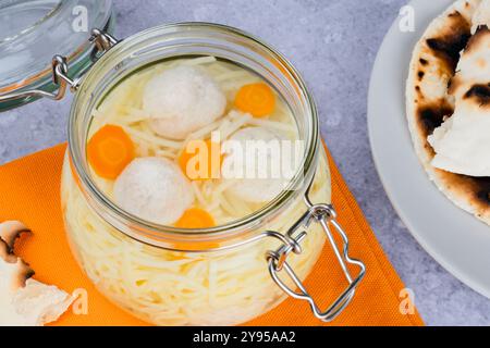 Matzoh-Bällchensuppe, Nudeln, lebendige Karotten auf grauem Hintergrund. Jüdische traditionelle Küche Passahessen. Gesundes festliches Essen. Draufsicht. Hohe Qualität Stockfoto