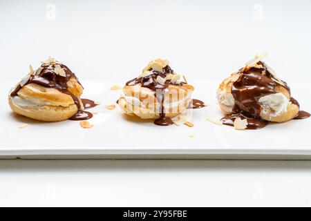 Profiteroles nach einem traditionellen französischen Rezept mit Vanillepudding, mit Schokolade getränkt und mit Mandelblättern auf weißem Hintergrund verziert. Hallo Stockfoto