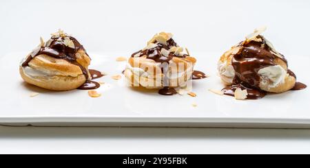 Profiteroles nach einem traditionellen französischen Rezept mit Vanillepudding, mit Schokolade getränkt und mit Mandelblättern auf weißem Hintergrund verziert. Hallo Stockfoto