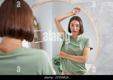 Emotionale Frau im T-Shirt vor der Verwendung von Deodorant in der Nähe des Spiegels zu Hause Stockfoto