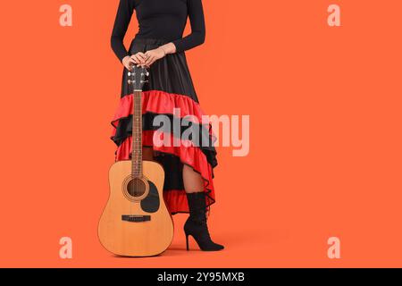 Junge Frau mit Gitarre auf orangem Hintergrund. Feierlichkeiten zum mexikanischen Todestag (El Dia de Muertos) Stockfoto