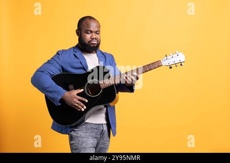 BIPOC man stimmt Gitarre, bevor er Songs während des Konzerts aufführt, isoliert über Studiohintergrund. Ein verärgerter Künstler, der nicht zufrieden ist mit einem verstimmten akustischen Musikinstrument, das es repariert Stockfoto