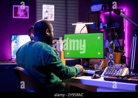 Songwriter arbeitet auf Synthesizer-Piano-Tasten neben einem isolierten Display und komponiert neue Musik mit Instrumenten und Stereo-Tools im Heimstudio. Der Artist Producer arbeitet mit Greenscreen. Stockfoto