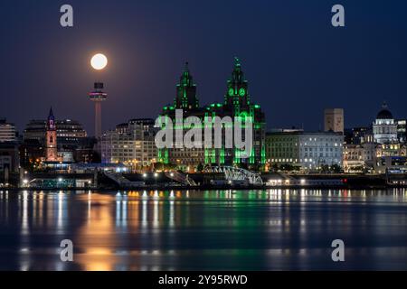 Ein Vollmond erhebt sich über dem Fluss Mersey und der Skyline von Liverpool, einschließlich des Wahrzeichens Royal Liver Building. Stockfoto