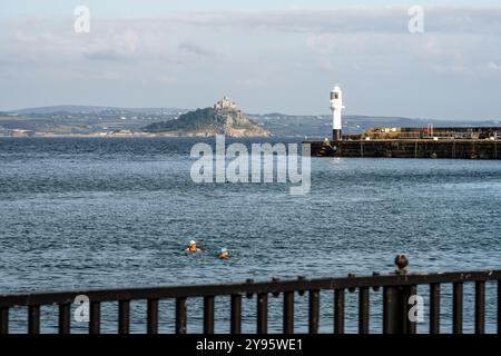 Zwei Personen schwimmen im Penzance Harbour, hinter dem sich der St. Michael's Mount erhebt, an der Küste von Cornwall. Stockfoto