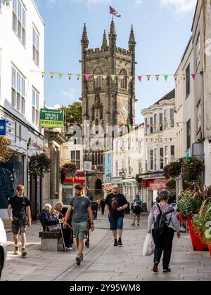 Die Menschen laufen entlang der Fore Street, der Haupteinkaufsstraße im Stadtzentrum von St. Austell, mit der Pfarrkirche der Heiligen Dreifaltigkeit. Stockfoto