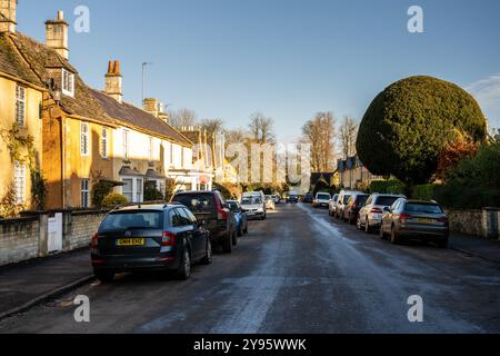 Parkende Autos und traditionelle Hütten säumen die High Street von Badminton Village in Englands Cotswolds. Stockfoto