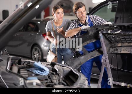 Interessierte Kundin, die Autoreparaturen mit einem Mechaniker bespricht Stockfoto