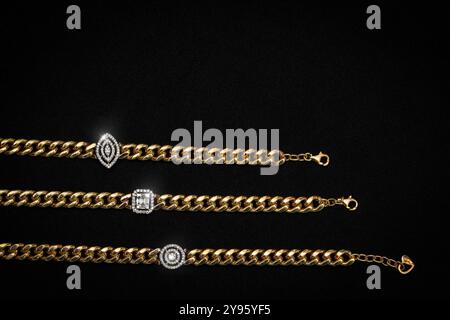 Ein luxuriöses Set aus drei goldenen Kettenarmbändern, jedes mit einem einzigartigen diamantbesetzten Anhänger in verschiedenen Formen: Auge, quadratisch und rund. Diese br Stockfoto