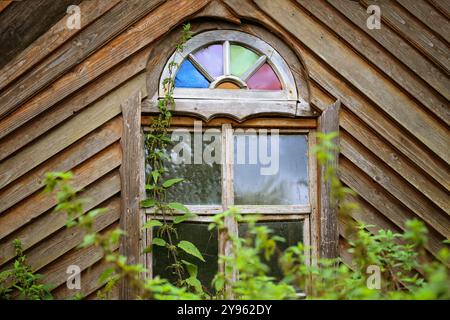 Fenster mit halbrunder farbiger Oberseite in einem selbstgebauten Holzschuppen mit diagonalen Diagonalen an der Fassade in einem wilden Naturgarten, Kopierraum, ausgewähltes foc Stockfoto