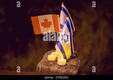 Toronto, Ontario, Kanada. Oktober 2024. Während der Demonstration auf dem Sherman Campus werden neben zündeten Kerzen auf einem Straßentrenner Flagge aus Israel und Kanada gesehen. Jüdische Gemeinden auf der ganzen Welt markierten den 7. Oktober, den tödlichsten Tag für das jüdische Volk seit dem Holocaust. Die UJA (United Jewish Appeal) Federation organisierte die Veranstaltung „7. Oktober: Marking One Year“ in Toronto, Kanada mit Gemeindemitgliedern, Verbündeten und Angehörigen von Geiseln, um Geschichten zu teilen, Kerzen anzuzünden und zusammen zu stehen, um die Ermordeten zu betrauern und die Überlebenden zu ehren. (Credit Image: © Shawn Goldberg/SOPA Images via ZUMA P Stockfoto