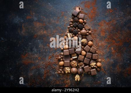 Schokolade und Pralinen in Form eines Weihnachtsbaums auf dunklem Schiefergrund, saisonale Weihnachtssüße, Blick von oben, großer Kopierraum Stockfoto