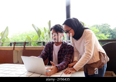 Zwei junge asiatische Arbeitskräfte, die am Cafe-Tisch diskutieren, mit Laptop arbeiten und Datei auf dem Bildschirm erklären Stockfoto