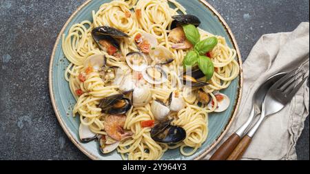 Italienische Meeresfrüchte-Pasta-Spaghetti mit Muscheln, Garnelen, Venusmuscheln in Tomatensoße mit grünem Basilikum auf Teller auf rustikalem blauem Betonhintergrund. Ich Stockfoto