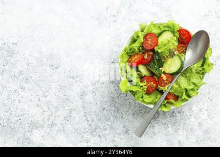 Gesunder Gemüsesalat mit frischen Gurken, Tomaten, frischen Eisbergsalatblättern in einer Schüssel auf rustikalem weißem Beton mit einem Löffel. Ve Stockfoto