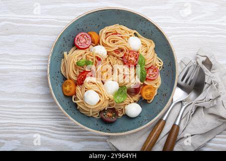 Köstliche Spaghetti mit Mozzarella, farbenfrohe Kirschtomaten, frisches Basilikum auf Keramikplatte auf rustikalem weißen Holzhintergrund mit Blick von oben. Italienische Heilkunst Stockfoto