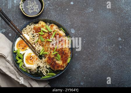 Asiatische Nudeln Ramen-Suppe mit frittiertem Panko-Hähnchenfilet und gekochten Eiern in einer Keramikschüssel mit Koteletts und Sojasauce auf rustikalem Backgroun aus Stein Stockfoto