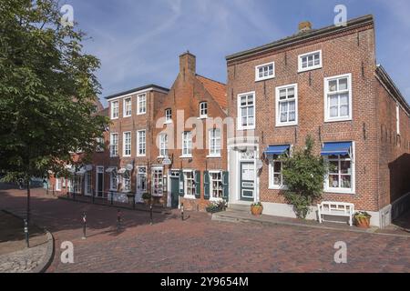 Backsteinhäuser entlang einer Kopfsteinpflasterstraße bei sonnigem Wetter, historisches Stadtzentrum mit Bäumen und Fenstern, fröhliche Atmosphäre, Fischerdorf Greetsiel, Kru Stockfoto