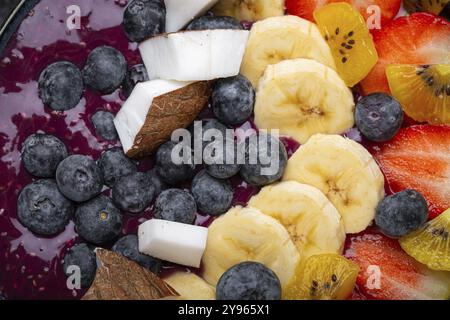 Gesunder Sommer Acai Smoothie Bowl mit Chiasamen, frischer Banane, Erdbeere, Heidelbeere, kokos, kiwi-Blick von oben auf rustikalem Betonhintergrund mit Löffel Stockfoto