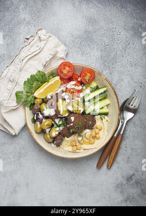 Falafel Salatschale mit Hummus, Gemüse, Oliven, Kräutern und Joghurtsauce. Vegane Mittagsplatte, Blick von oben auf rustikalen Steinhintergrund, gesunde Mahlzeit mit f Stockfoto