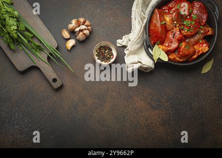 Kochen von Fleischeintopf. Rohe, nicht gekochte, gehackte Fleischstücke, mariniert mit Gewürzen und Petersilie in schwarzer Auflaufform von oben, Schneidebrett, Zutat Stockfoto