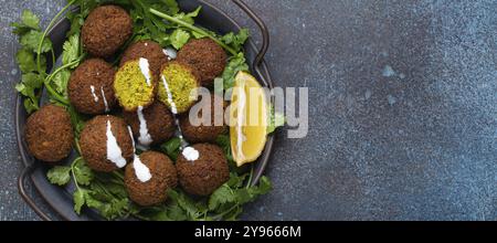 Teller mit gebratenen Falafel-Kugeln, serviert mit frischem grünem Koriander und Blick auf die Zitronenspitze auf rustikalem Betonhintergrund. Traditionelles veganes Gericht aus Middle Easte Stockfoto