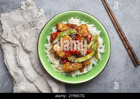 Asiatisches, süßsaures, klebriges Hühnchen mit Gemüse, Braten und Reis in einer Keramikschale mit Essstäbchen, Draufsicht auf grauem rustikalem Steinhintergrund, traditionell Stockfoto