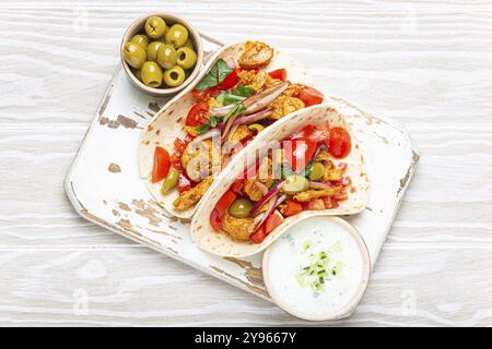 Traditionelles griechisches Gericht Gyros: Pita-Brot mit Gemüse, Fleisch, Kräutern, Oliven auf rustikalem Holzbrett mit Tzatziki-Sauce, Olivenölplatte Stockfoto