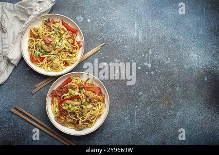 Zwei Schüsseln mit Chow mein oder Lo mein, traditionellen chinesischen Pfannennudeln mit Fleisch und Gemüse, serviert mit Essstäbchen von oben auf rustikalem blauen Coffee Stockfoto