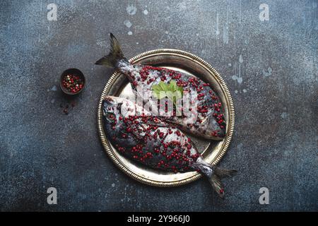 Zwei rohe Fische dorado, gewürzt in pinkfarbenem Pfefferkorn, fertig zum Kochen, auf rustikalem Metallblech, Draufsicht. Gesundes Kochen, Diät Essen Konzept. Stockfoto