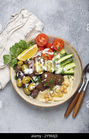 Falafel Salatschale mit Hummus, Gemüse, Oliven, Kräutern und Joghurtsauce. Vegane Mittagsplatte, Blick von oben auf rustikalen Steinhintergrund, gesunde Mahlzeit mit f Stockfoto