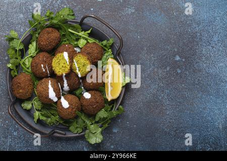 Teller mit gebratenen Falafel-Kugeln, serviert mit frischem grünem Koriander und Blick auf die Zitronenspitze auf rustikalem Betonhintergrund. Traditionelles veganes Gericht aus Middle Easte Stockfoto