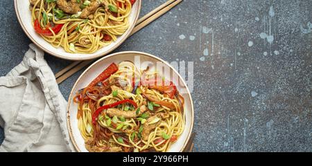 Zwei Schüsseln mit Chow mein oder Lo mein, traditionellen chinesischen Pfannennudeln mit Fleisch und Gemüse, serviert mit Essstäbchen von oben auf rustikalem blauen Coffee Stockfoto