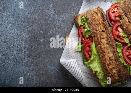 Zwei dunkle Ciabatta-Sandwiches mit grünem Salat, reifen roten Tomaten, Zwiebeln und Thunfisch auf rustikalem Betonstein mit Blick von oben. Vegetarische Sa mit Gemüse Stockfoto