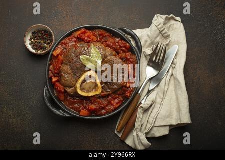 Traditionelles italienisches Gericht Ossobuco alles Milanese mit geschnittenem Kalbsschenkelfleisch mit Gemüsetomatensauce serviert in schwarzer Auflaufpfanne mit Blick von oben auf rus Stockfoto