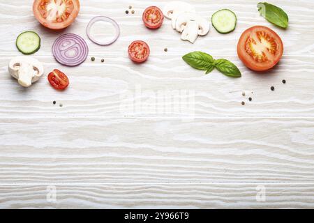 Hintergrund der Speisenzubereitung: Frisch zubereitete Zutaten, Basilikum, Kirschtomaten, Pilze, geschnittene Gurken, Zwiebel, Chili-Pfeffer, Gewürze auf weißem Holzbalken Stockfoto