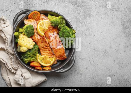 Gesunde gebackene Fischlachssteaks, Brokkoli, Blumenkohl, Karotte in einer schwarzen gusseisernen Auflaufschale auf grauem Steinhintergrund. Kochen Sie eine köstliche niedrige Ca Stockfoto