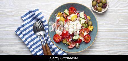 Griechischer frischer, gesunder, farbenfroher Salat mit Fetakäse, Gemüse, Oliven in blauer Keramikschüssel auf rustikalem weißem Holzhintergrund mit Blick von oben, mediterrane Küche Stockfoto