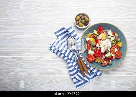 Griechischer frischer, gesunder, farbenfroher Salat mit Fetakäse, Gemüse, Oliven in blauer Schüssel auf rustikalem weißem Holzhintergrund, Blick von oben, mediterrane Diät, t Stockfoto