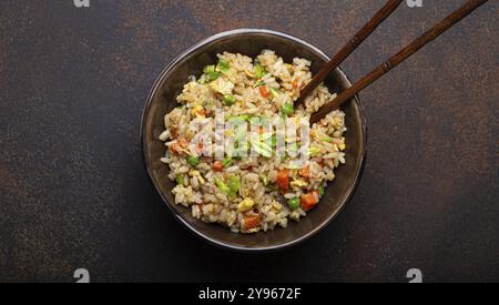 Authentischer chinesischer und asiatischer gebratener Reis mit Ei und Gemüse in brauner Keramikschale auf dunklem rustikalem Betontischhintergrund. Traditionelles di Stockfoto