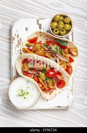 Traditionelles griechisches Gericht Gyros: Pita-Brot mit Gemüse, Fleisch, Kräutern, Oliven auf rustikalem Holzbrett mit Tzatziki-Sauce, Olivenölplatte Stockfoto