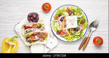 Traditionelles griechisches Essen: Griechischer Salat, Gyros mit Fleisch und Gemüse, Tzatziki-Sauce, Oliven auf weißem rustikalem Holztisch mit Blick von oben. Küche Stockfoto