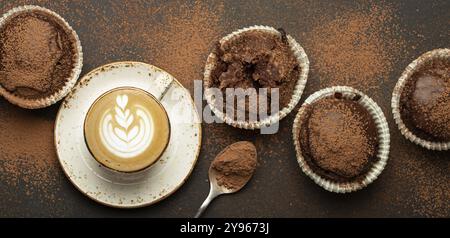 Schokolade und Kakao bräunliche Muffins mit Kaffee Cappuccino in der Tasse von oben auf braunem rustikalem Steinhintergrund, süße hausgemachte dunkle Schokolade Cupcakes, fo Stockfoto