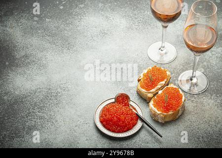 Kleine Metallplatte mit rotem Lachskaviar, zwei Kaviar Toast Canape, zwei Gläser Champagner von oben auf grauem Betonhintergrund, festlicher Luxus-Feinkost Stockfoto