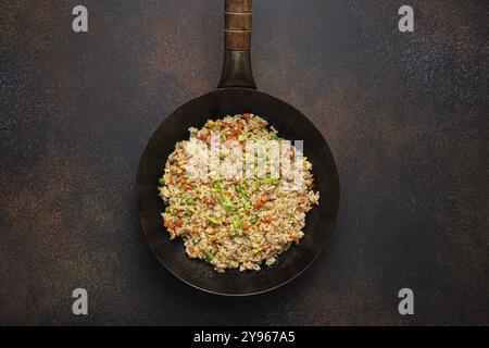 Authentischer chinesischer und asiatischer gebratener Reis mit Ei und Gemüse im Wok-Blick von oben auf rustikalem Betontischhintergrund. Traditionelles Gericht aus China, Lebensmittel ph Stockfoto